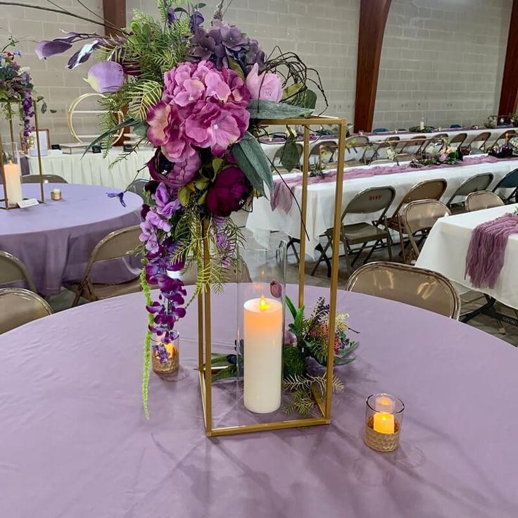 purple flowers and greenery in a gold frame on a round table with white linens