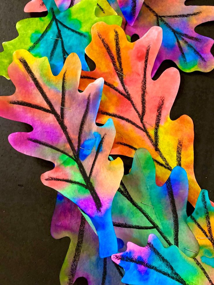 some colorful leaves are laying on the ground with one leaf painted in different colors and shapes