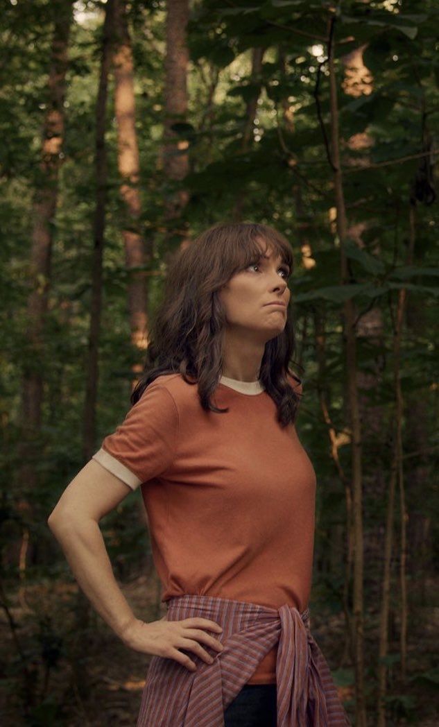 a woman standing in the woods with her hands on her hips