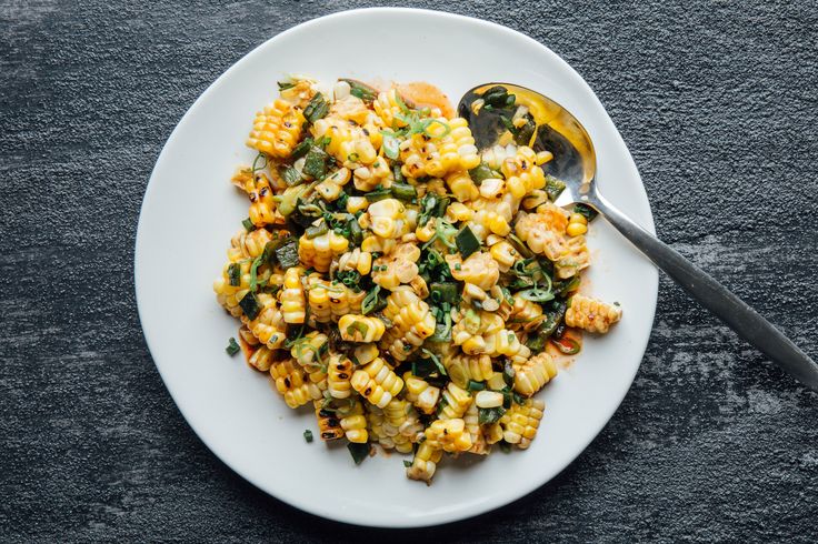 a white plate topped with corn and spinach next to a spoon on top of a table