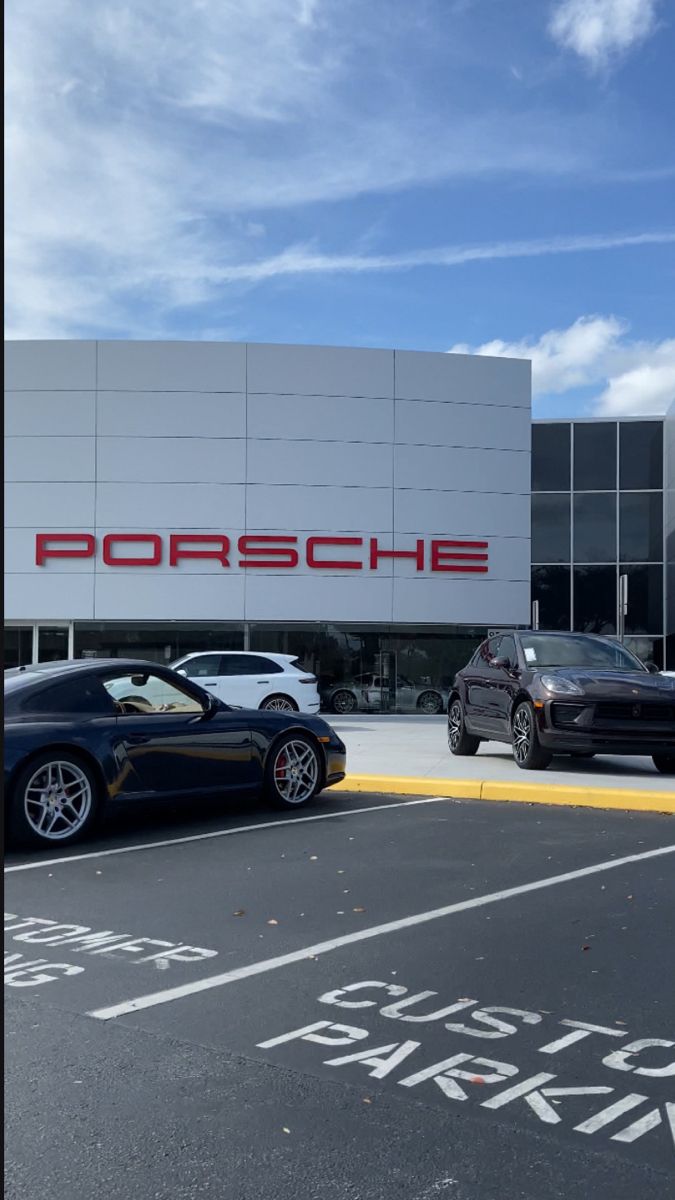 two cars parked in front of a porsche dealership with the word porsche on it