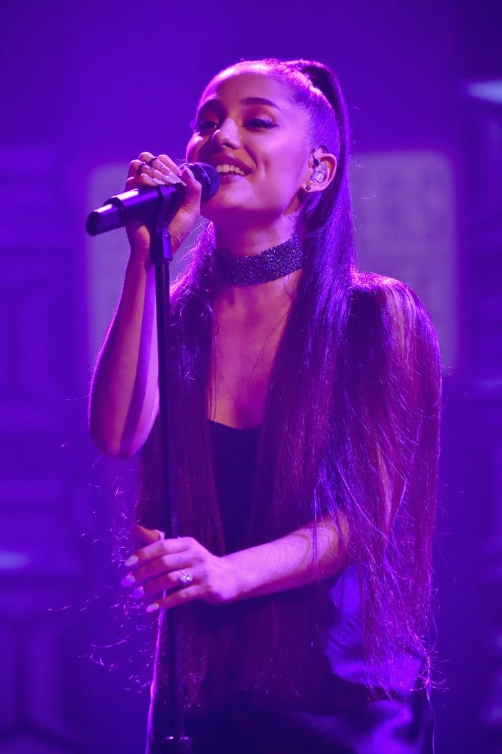 a woman singing into a microphone in front of purple lights on the side of a stage