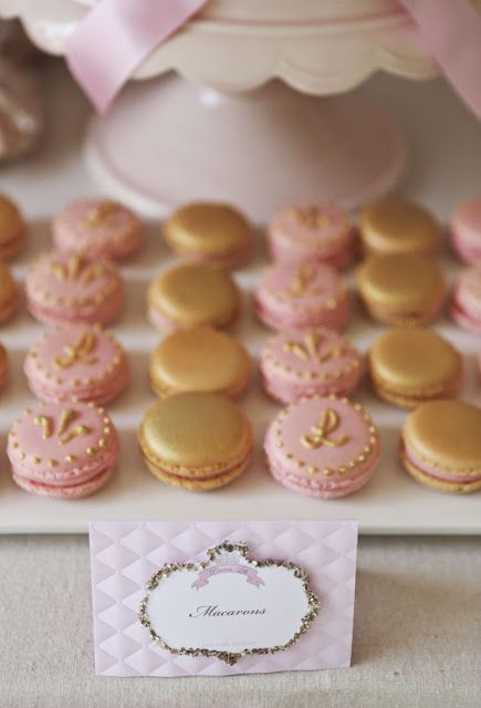 some pink and gold decorated cookies on a white table with cupcakes in the background