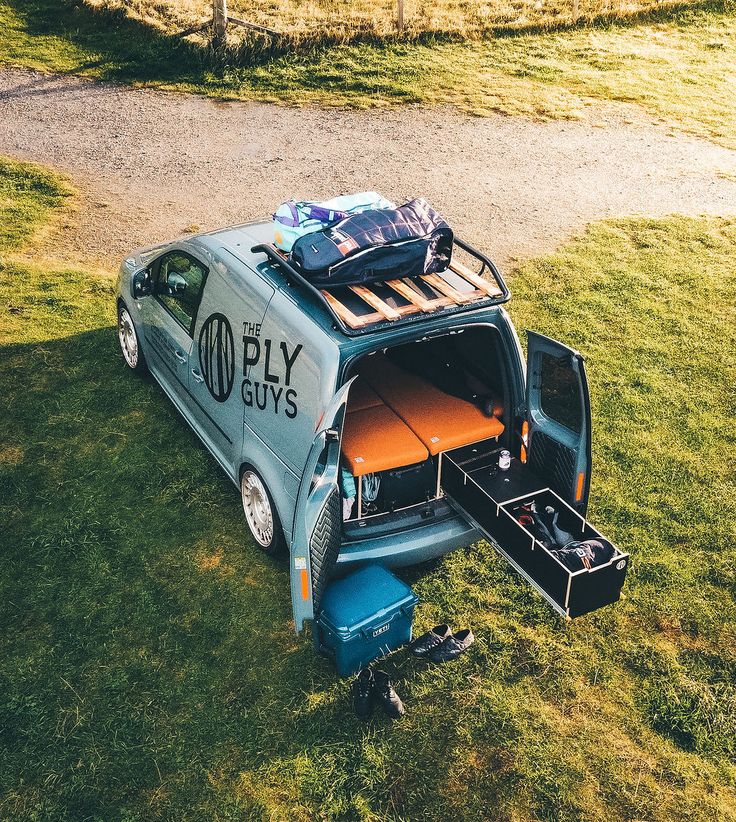 an old car with luggage in the back parked on grass next to a path and dirt road