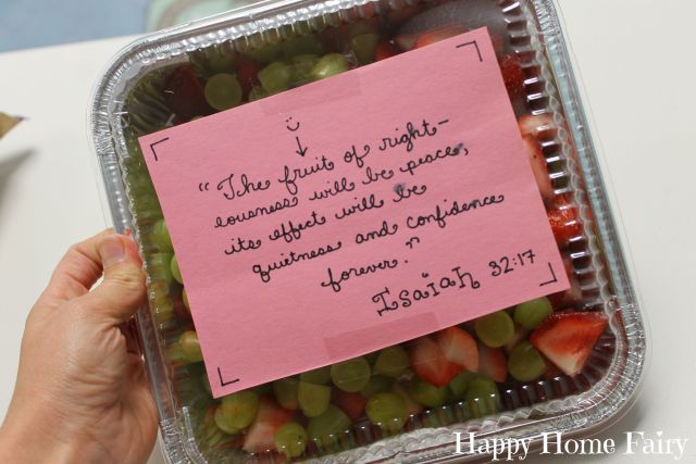 a hand holding a container filled with grapes and strawberries next to a piece of pink paper