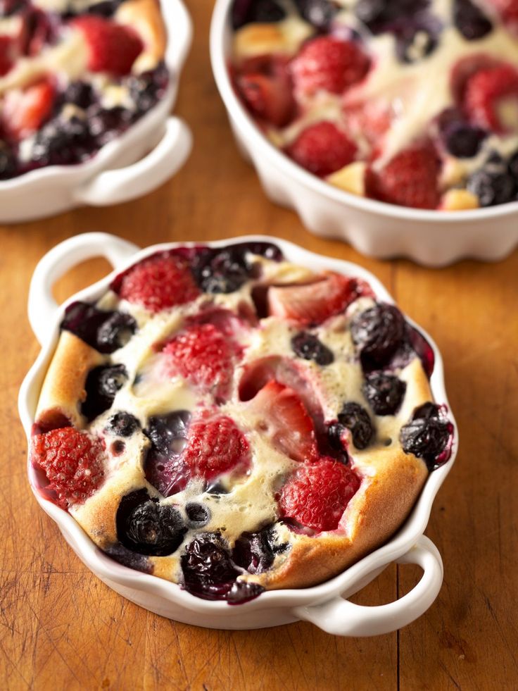 a dessert dish with berries and blueberries in it on a wooden table next to other dishes