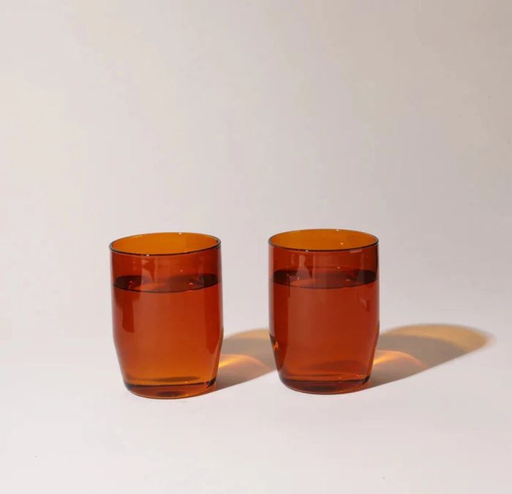 two orange glass cups sitting next to each other on a white surface with the light shining through them