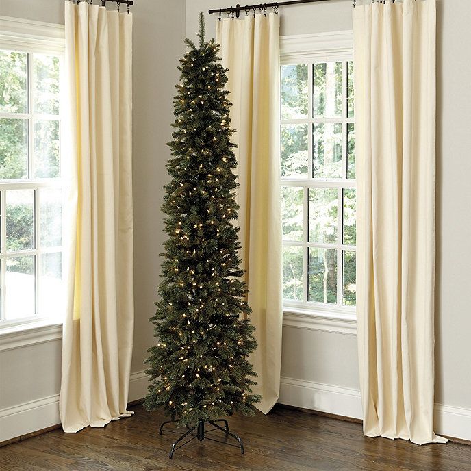 a christmas tree is in the corner of a room with two windows and drapes