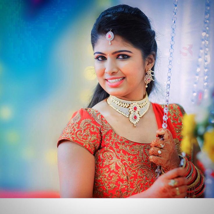 a woman in an orange and gold sari holding a necklace on her neck, smiling at the camera