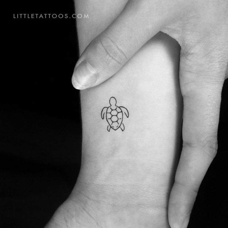 a small turtle tattoo on the left wrist is shown in black and white, with an outline