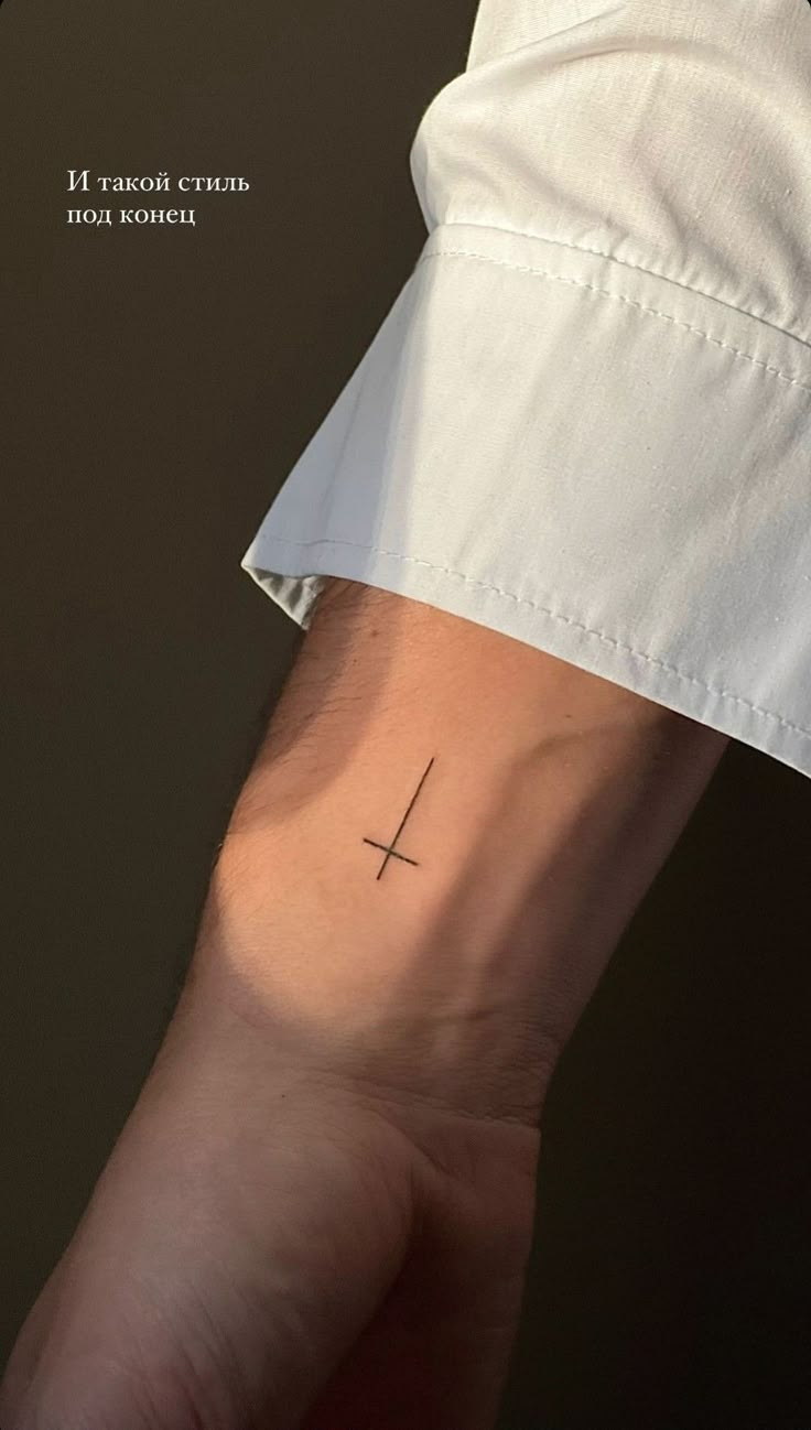 a person's arm with a small cross tattoo on the left side of their wrist