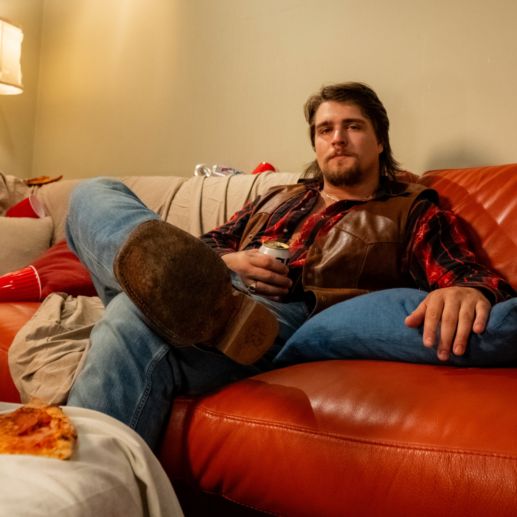 a man sitting on top of a red couch next to a pizza and a lamp