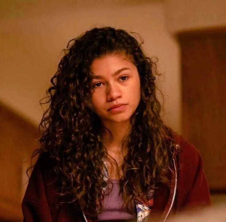 a woman with long curly hair is looking at the camera while wearing a red jacket