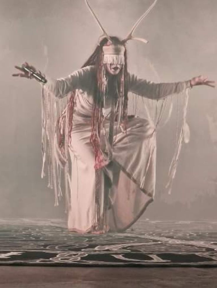 a woman dressed in white with long hair and horns on her head is dancing while holding two hands out