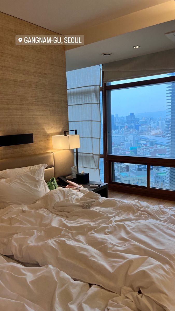 an unmade bed in a hotel room with a large window overlooking the cityscape