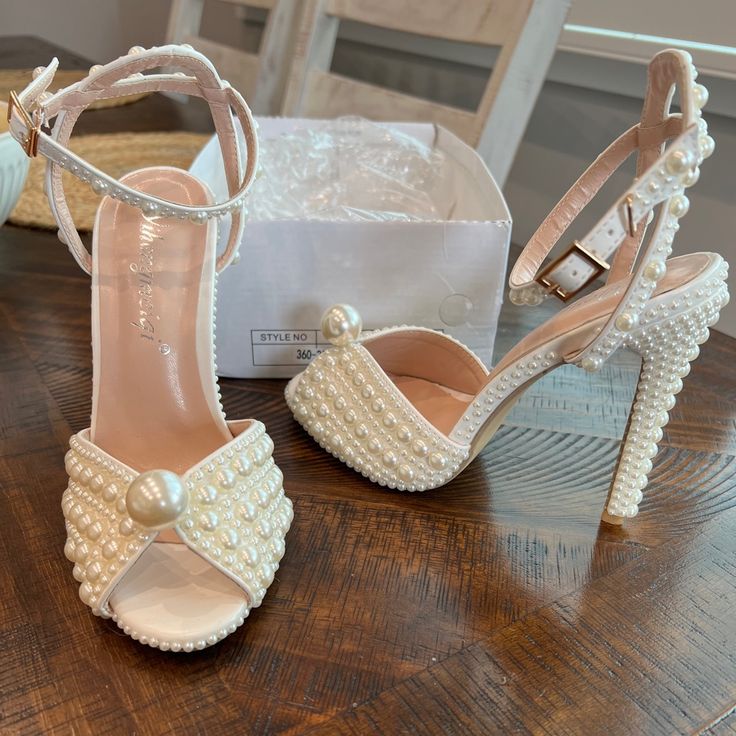 a pair of white high heeled shoes sitting on top of a wooden table next to a box