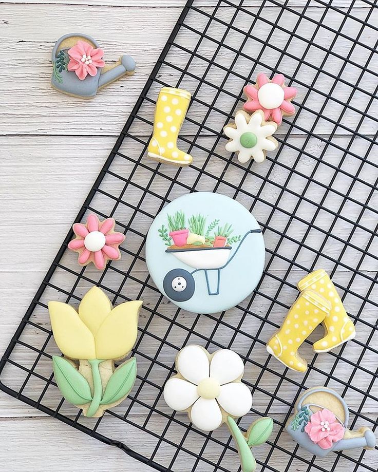 decorated cookies sitting on top of a cooling rack next to flowers and watering equipment,