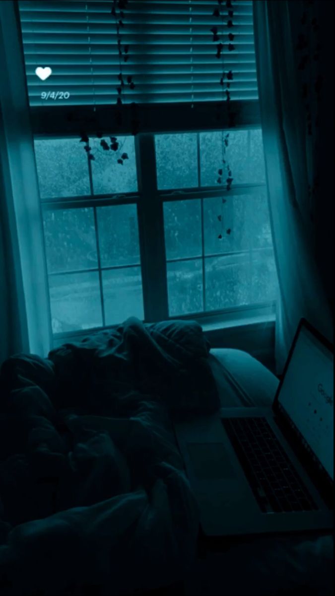 a laptop computer sitting on top of a bed under a window in a dark room