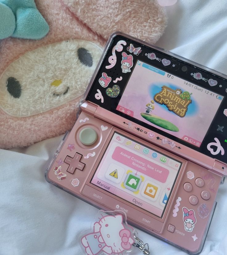 a pink nintendo wii game system sitting on top of a bed next to a stuffed animal