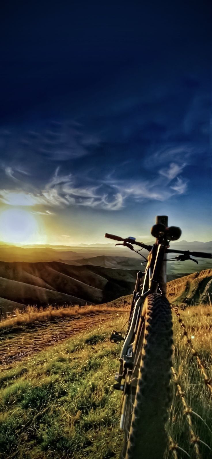 a bike parked on top of a lush green hillside under a blue sky with clouds