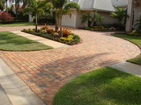 a brick driveway surrounded by palm trees and landscaping