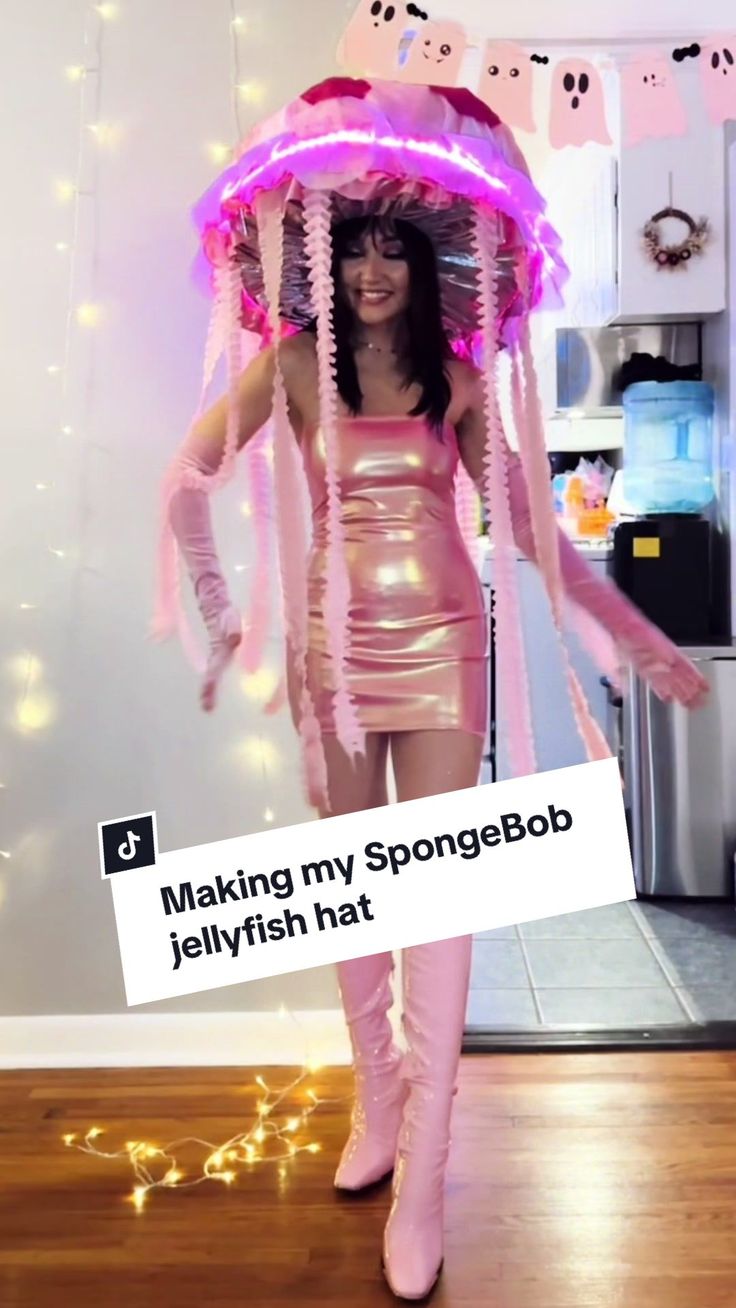 a woman dressed in pink is holding a jellyfish hat while standing on the floor