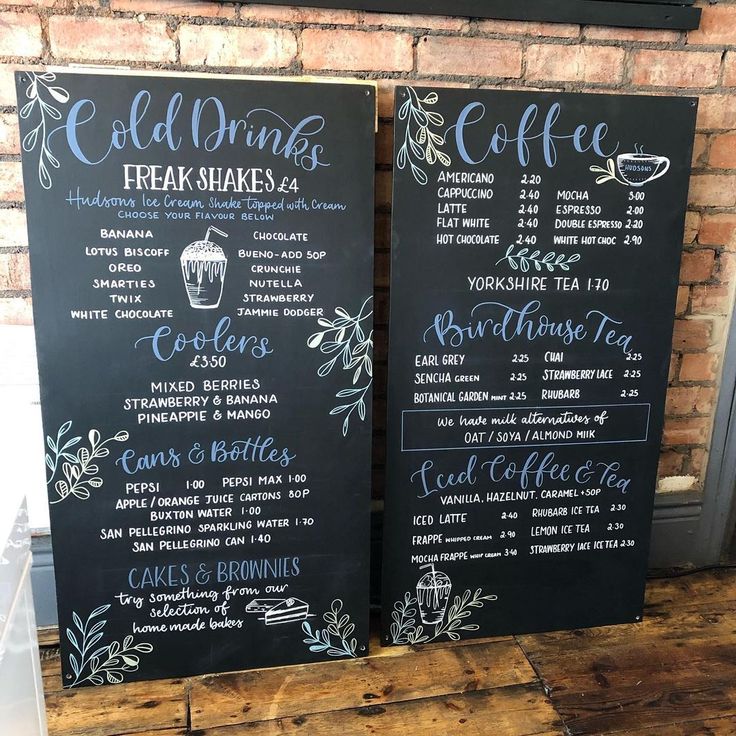 two chalkboard menus sitting on top of a wooden table next to a brick wall