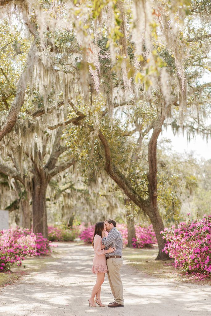 an engaged couple kissing under the spanish moss covered trees at their engagement session in charleston, sc