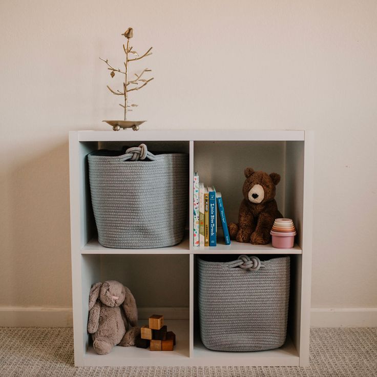 a teddy bear sitting on top of a white shelf next to baskets and stuffed animals