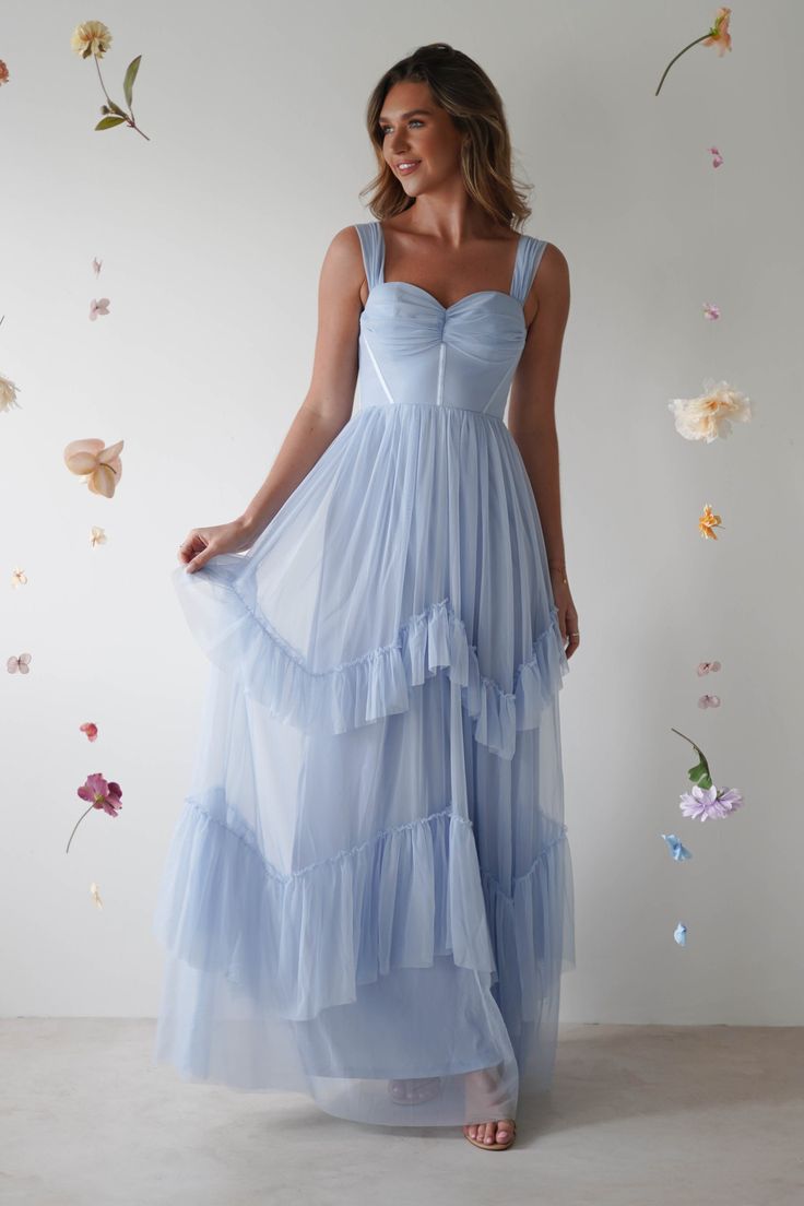 a woman wearing a blue dress standing in front of a wall with flowers on it