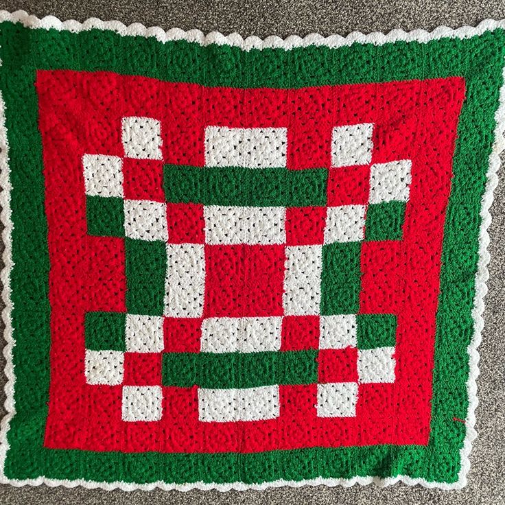 a red and green crocheted afghan with white squares on it's edges