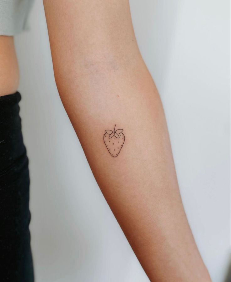 a woman's arm with a small tattoo of a strawberry on the left forearm