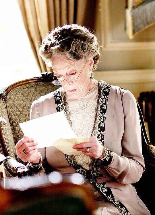 an older woman sitting in a chair holding a piece of paper and looking at it