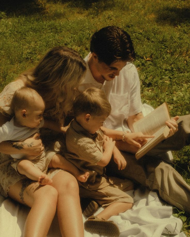 a woman and two children are sitting on the grass with an open book in their hands