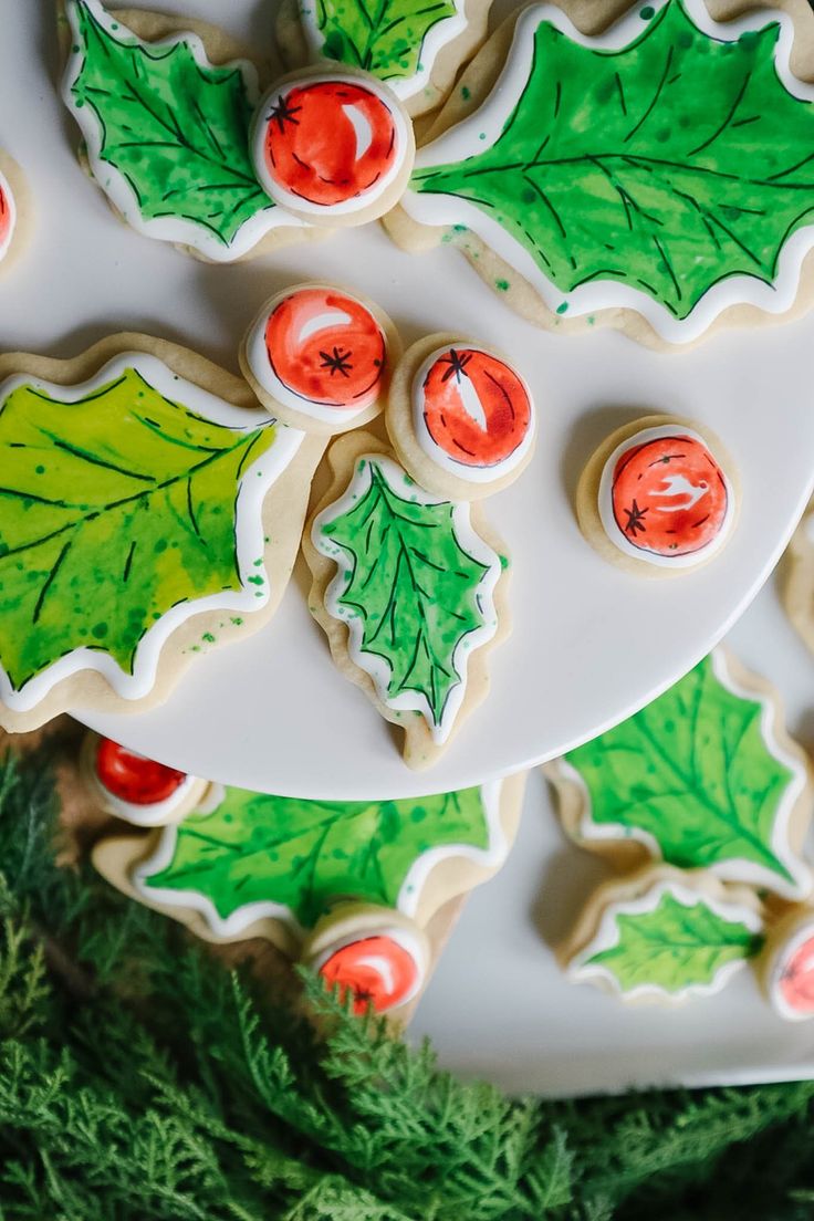 decorated christmas cookies on a platter with holly leaves