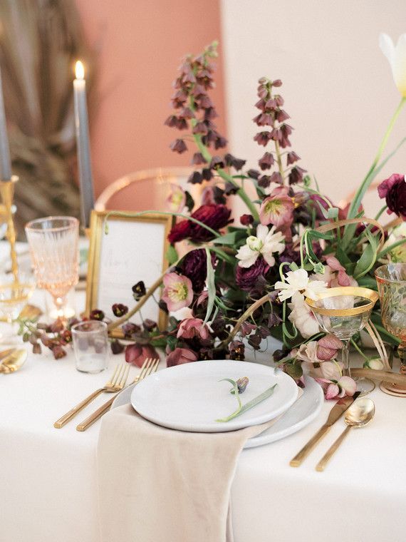 the table is set with white and purple flowers, gold place settings, and silverware