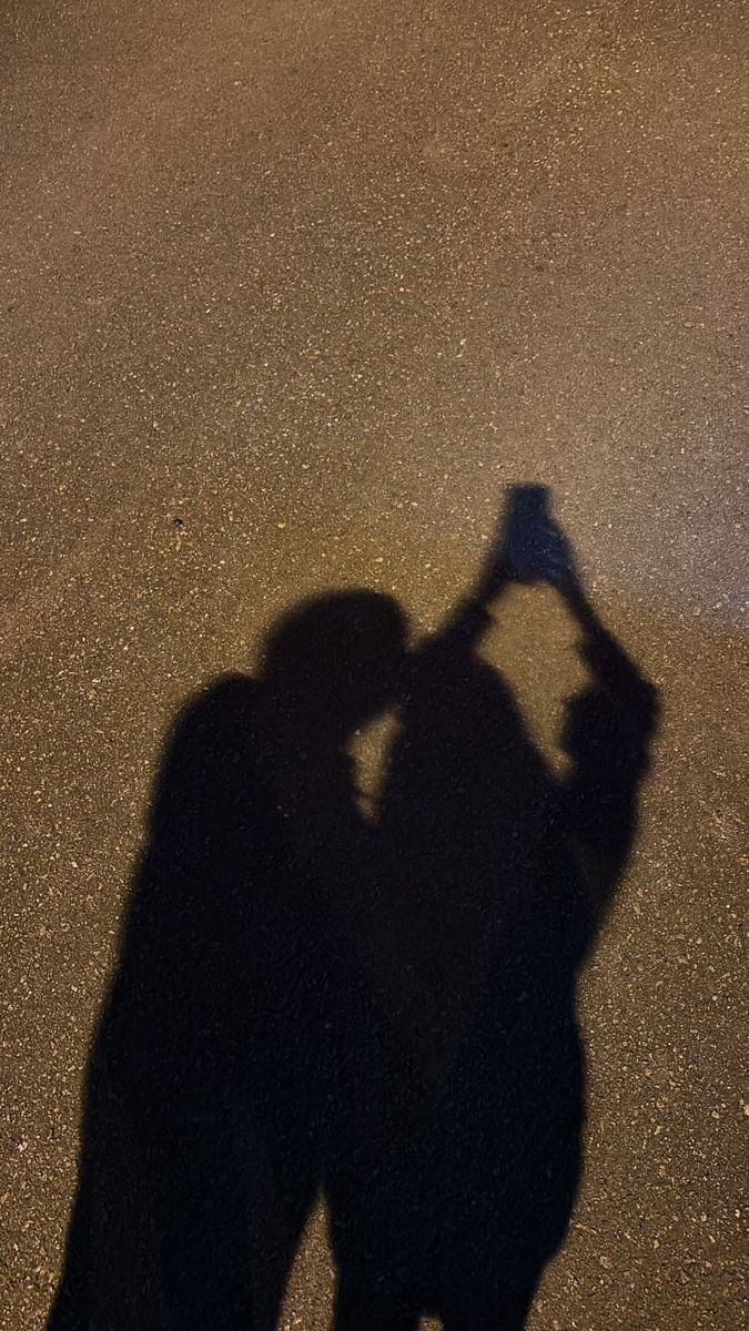 the shadow of a person holding a skateboard in their hand and standing on an asphalt surface