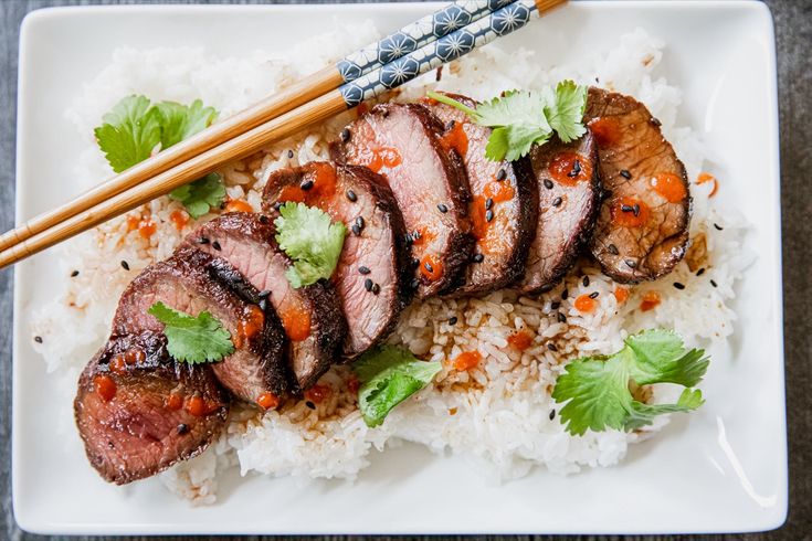 some meat and rice on a plate with chopsticks