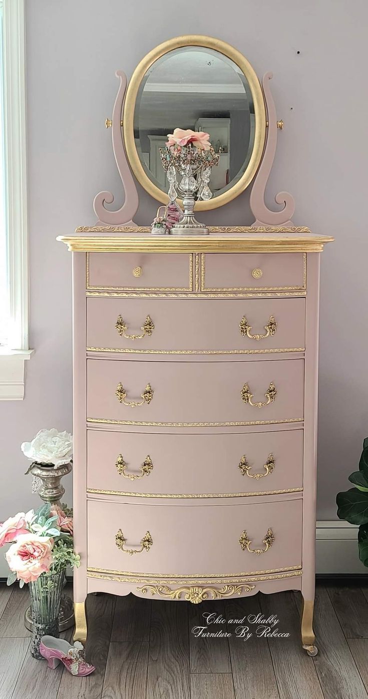 a pink dresser with a mirror on top of it next to a potted plant