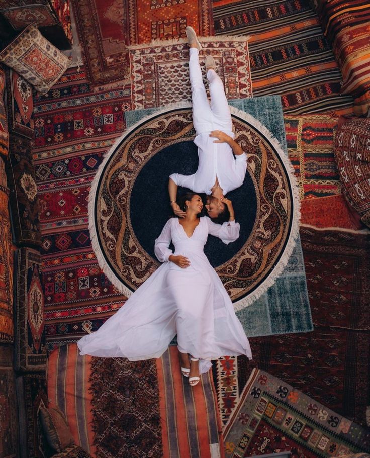 two people in white dress standing on rugs with their arms around each other and holding hands