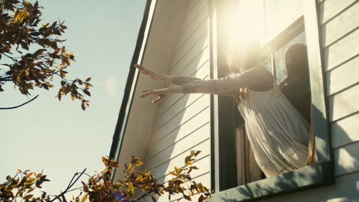 a woman standing on the outside of a window with her arms outstretched in the air