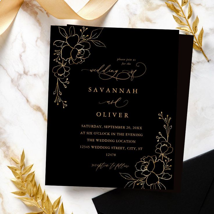 an elegant black and gold wedding card with flowers on the front is surrounded by golden leaves