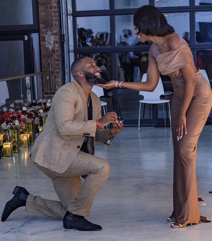 a man kneeling down next to a woman in a tan dress and black shoes on the floor