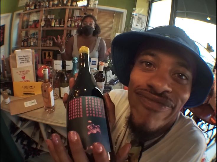 a man holding up a bottle of wine in front of a counter with bottles on it