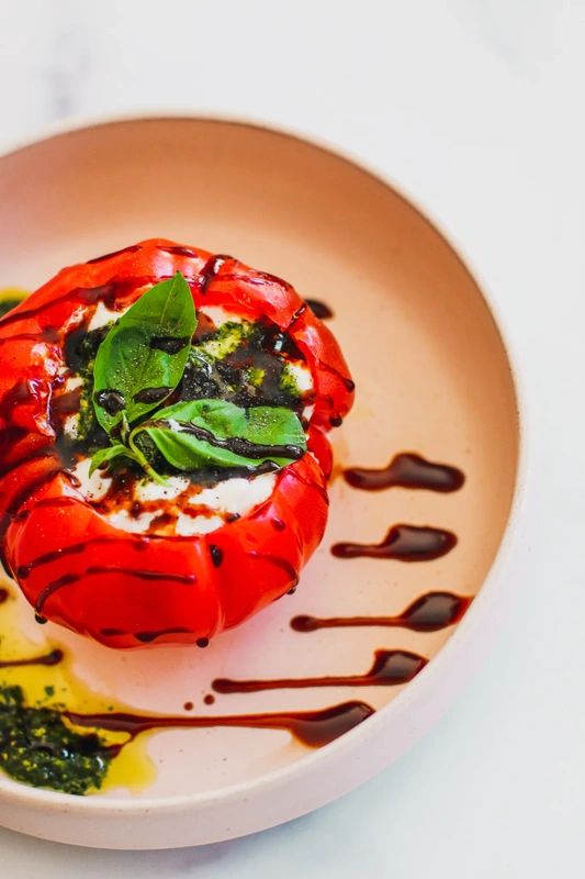 a plate topped with a stuffed red pepper covered in sauce and green leafy garnish