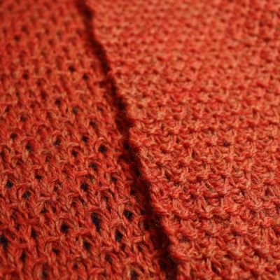 an orange crocheted blanket with black dots on it's edges is shown