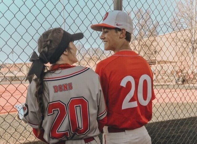 two baseball players standing next to each other in front of a fence and looking at each other