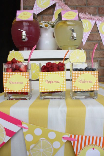 a table with lemons, raspberries and water in small glass vases