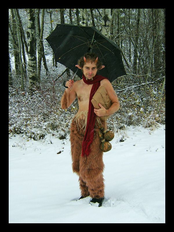 a man dressed up as a caveman holding an umbrella in the snow with trees behind him