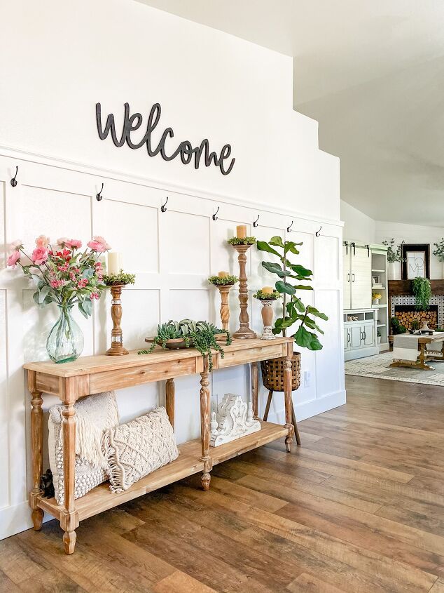 a welcome sign is on the wall above a wooden table with candles and flowers in vases